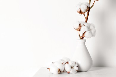 Photo of Cotton branch with fluffy flowers in vase on wooden table against white background. Space for text