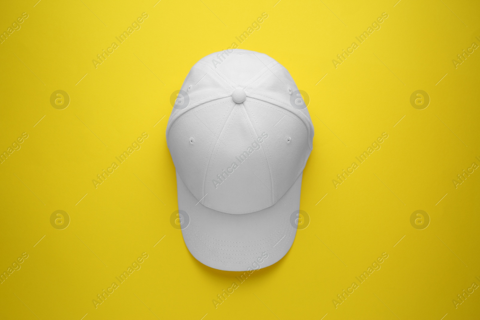 Photo of Stylish white baseball cap on yellow background, top view