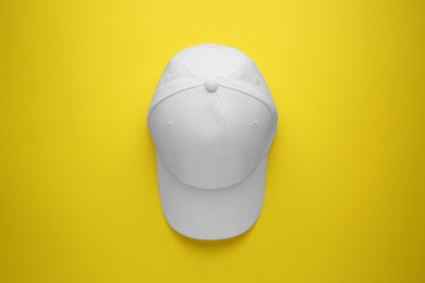 Photo of Stylish white baseball cap on yellow background, top view