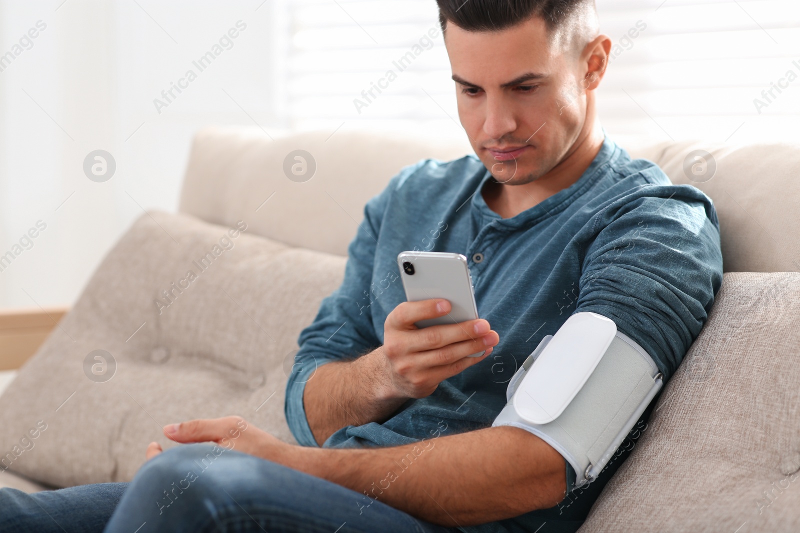 Photo of Man checking blood pressure with modern monitor and smartphone indoors