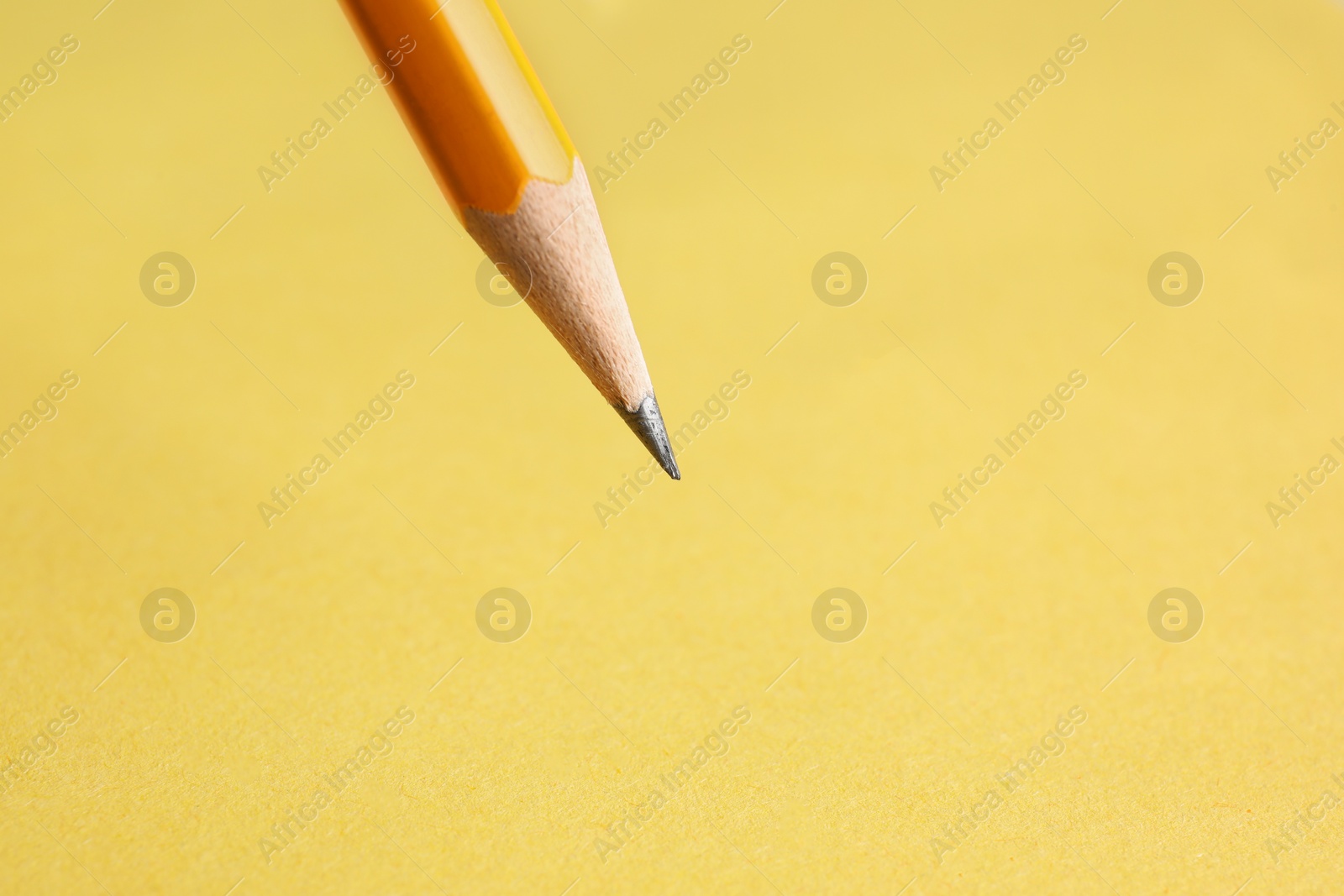 Photo of One sharp graphite pencil on yellow background, closeup. Space for text