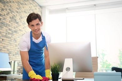 Photo of Young man in apron and gloves cleaning office