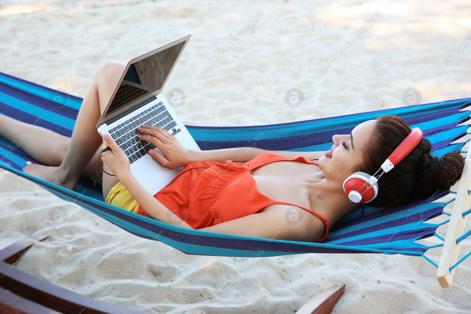 Photo of Young woman listening to music in comfortable hammock at seaside