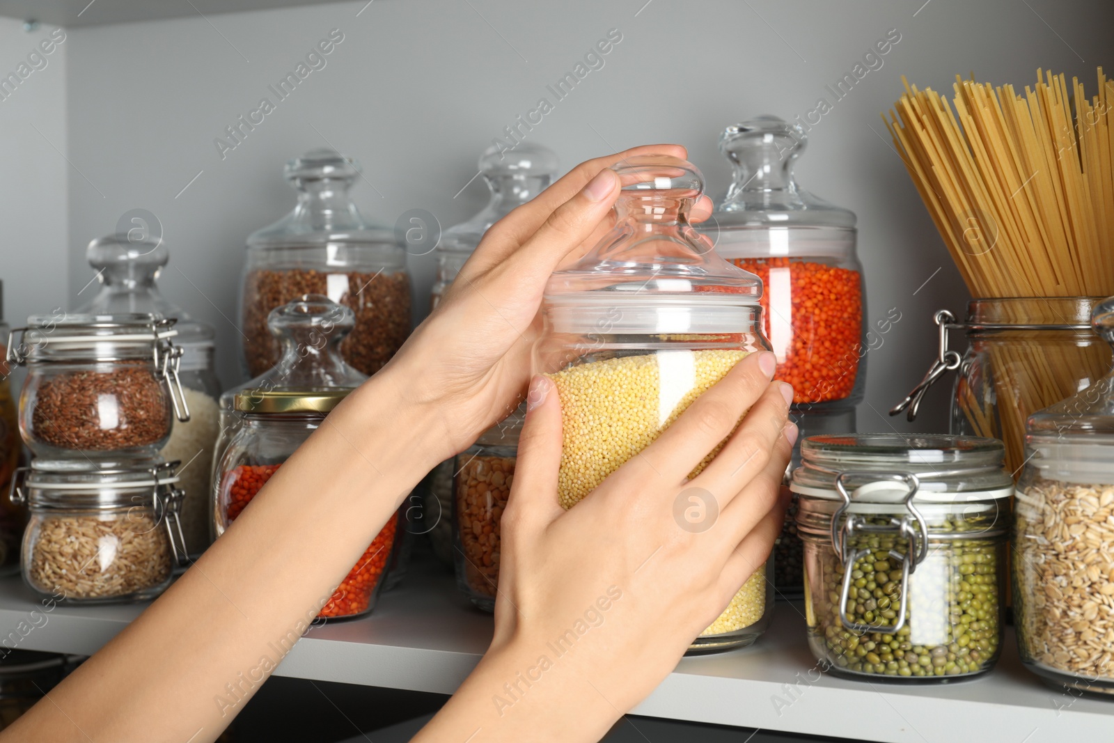 Photo of Woman taking jar of millet groat from white shelf, closeup