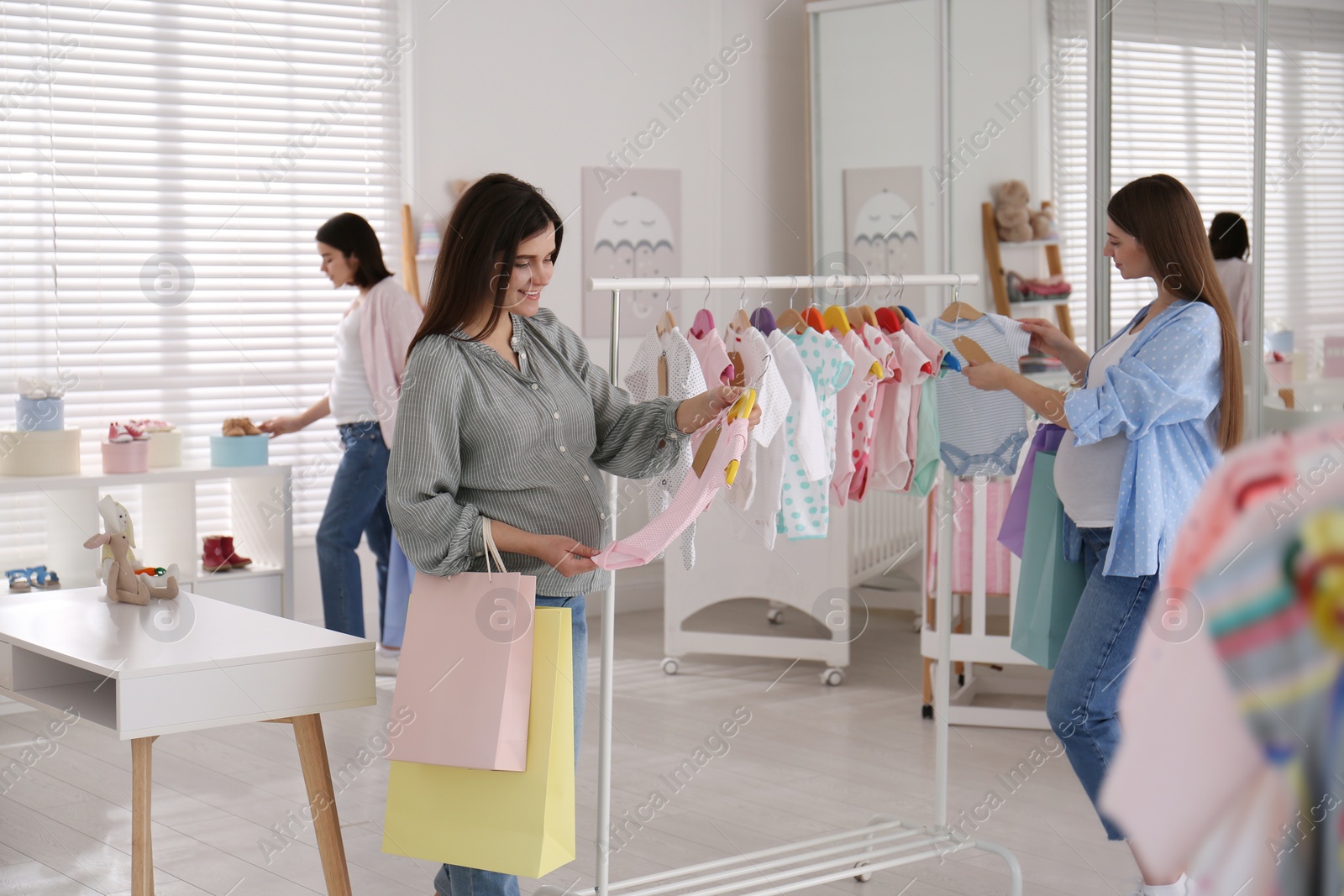 Photo of Happy pregnant women with shopping bags choosing baby clothes in store