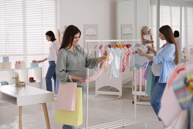 Happy pregnant women with shopping bags choosing baby clothes in store