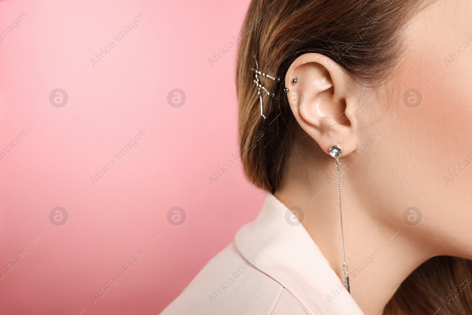 Photo of Young woman with ear piercing on pink background, closeup. Space for text