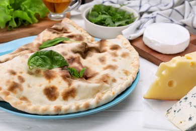 Photo of Delicious cheese calzones and products on white wooden table, closeup