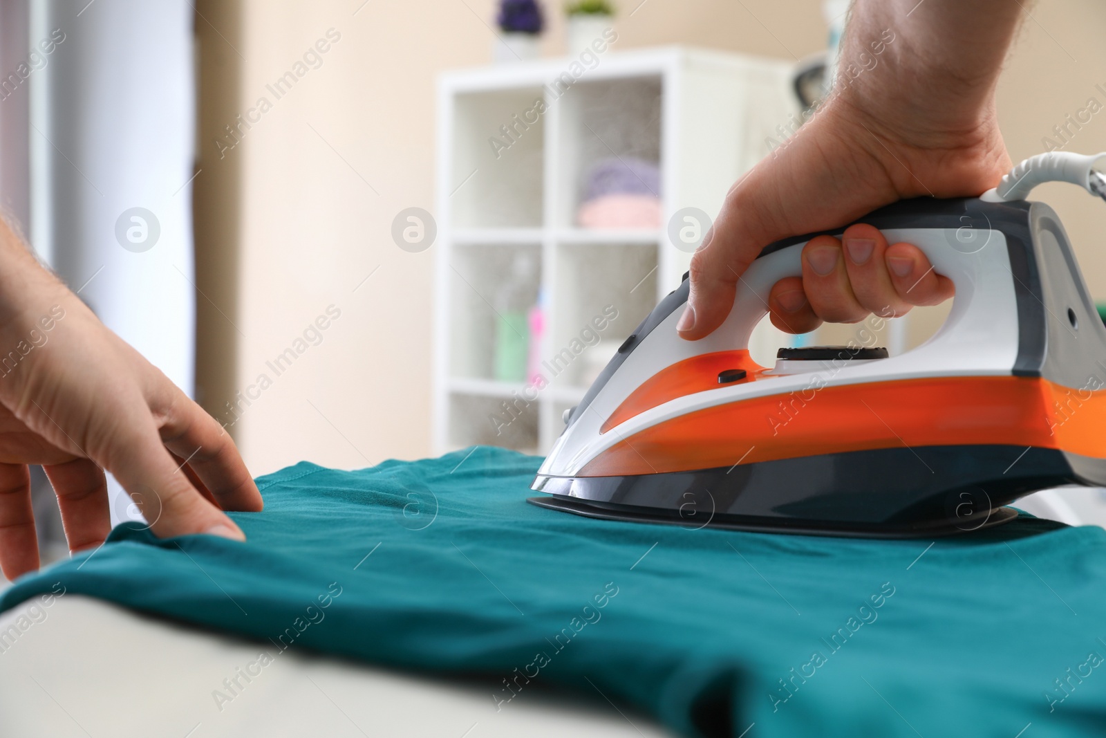 Photo of Man ironing clothes on board at home, closeup