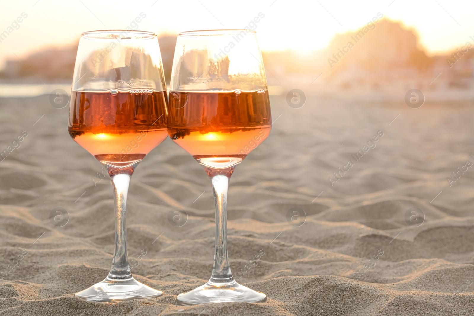 Photo of Glasses of tasty rose wine on sandy beach, space for text