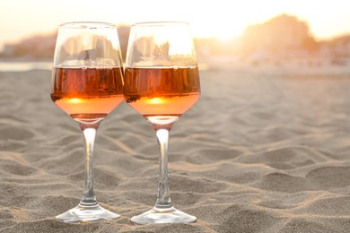 Photo of Glasses of tasty rose wine on sandy beach, space for text