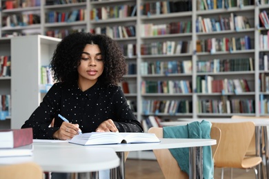 Photo of Young African-American woman studying at table in library
