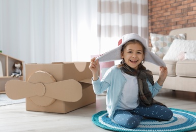Cute little girl playing with cardboard airplane in living room