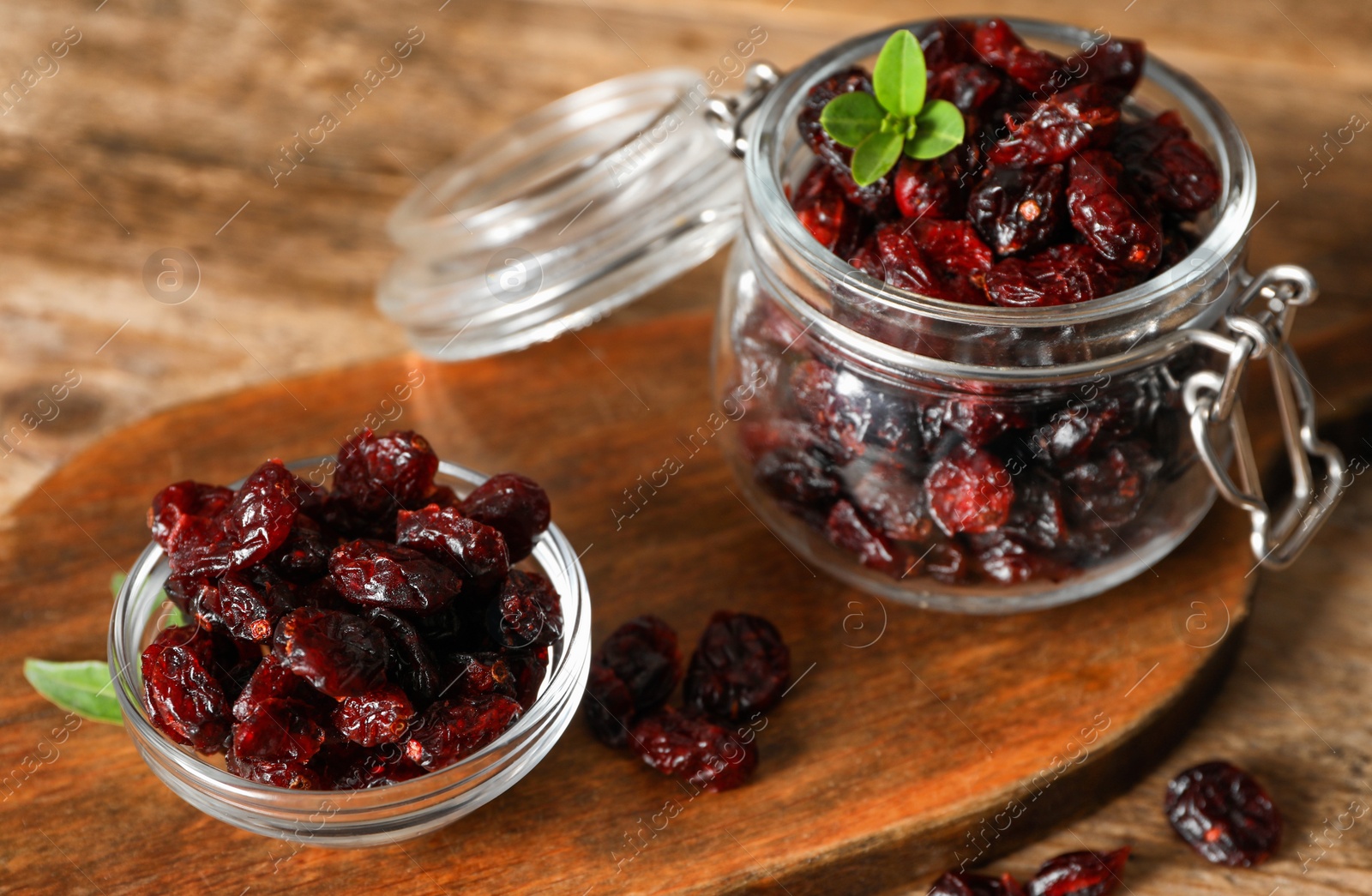 Photo of Tasty dried cranberries in glass bowl and jar on wooden table