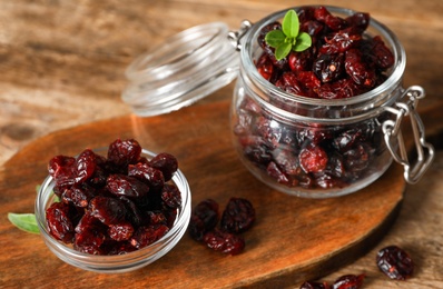 Tasty dried cranberries in glass bowl and jar on wooden table