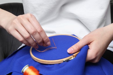 Photo of Woman with sewing needle and thread embroidering on cloth, closeup