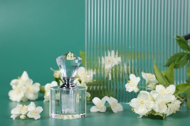 Photo of Aromatic perfume in bottle and beautiful jasmine flowers on green background