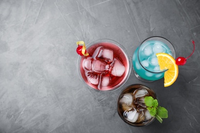 Photo of Tasty refreshing cocktails in glasses on grey stone table, flat lay. Space for text