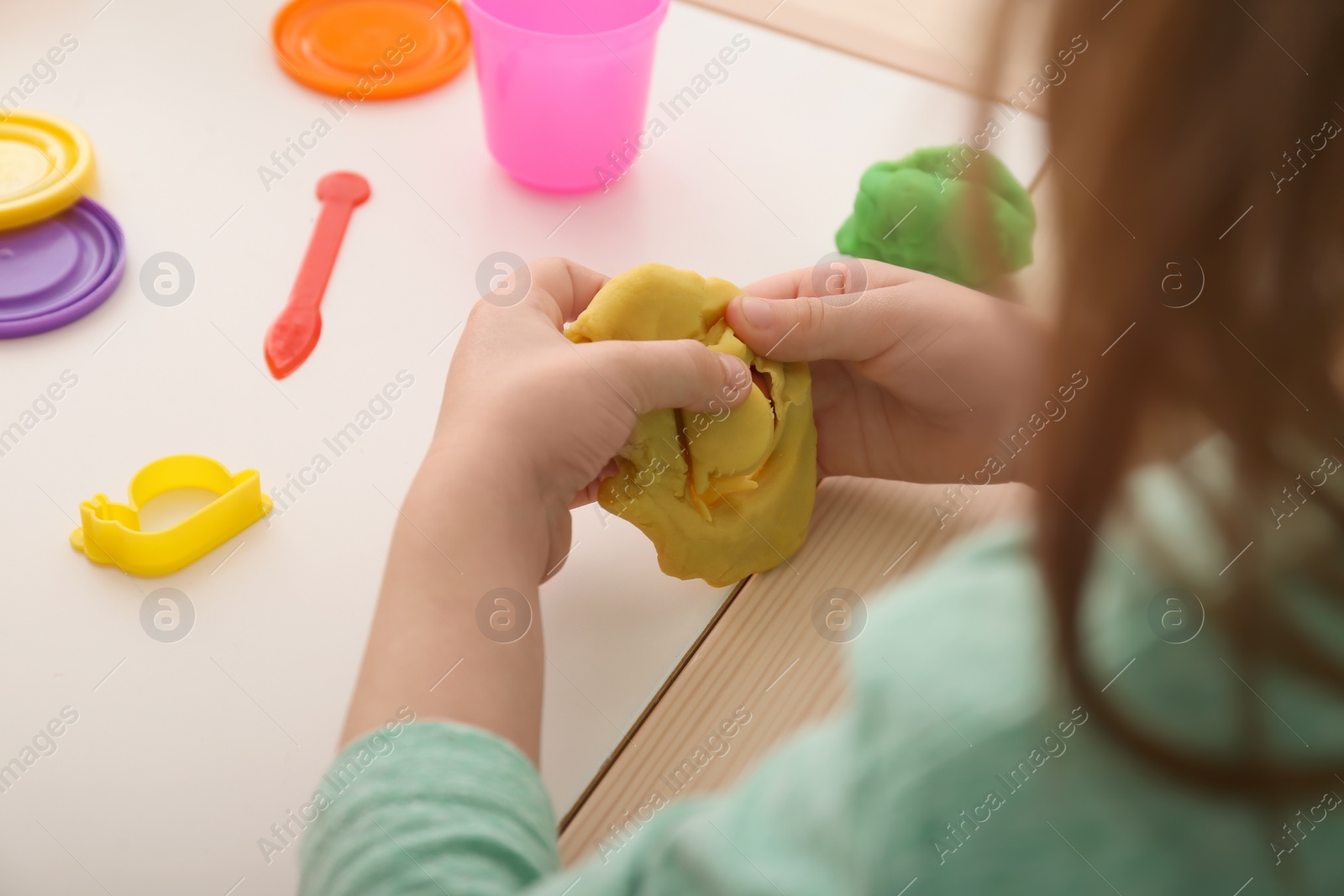 Photo of Cute little girl using play dough at table, closeup