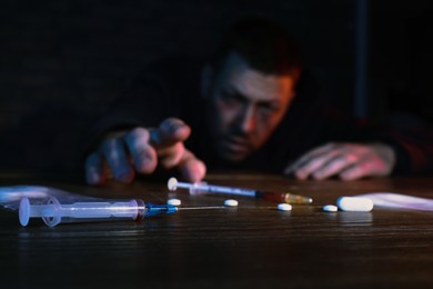 Photo of Addicted man reaching to drugs at table, focus on syringe