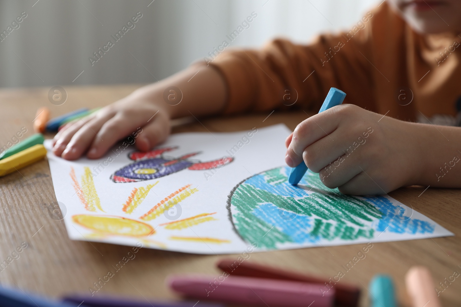 Photo of Little girl drawing picture with soft pastel at wooden table indoors, closeup. Child`s art