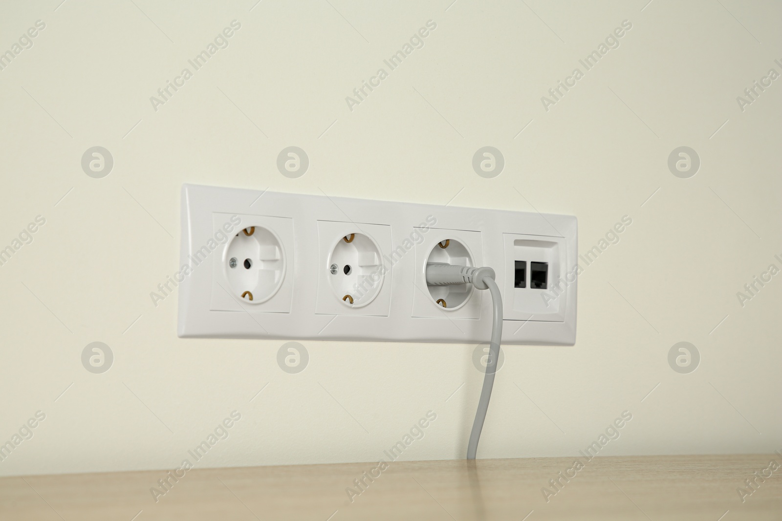 Photo of Many power sockets with plug and ethernet plate on white wall indoors