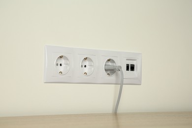 Photo of Many power sockets with plug and ethernet plate on white wall indoors