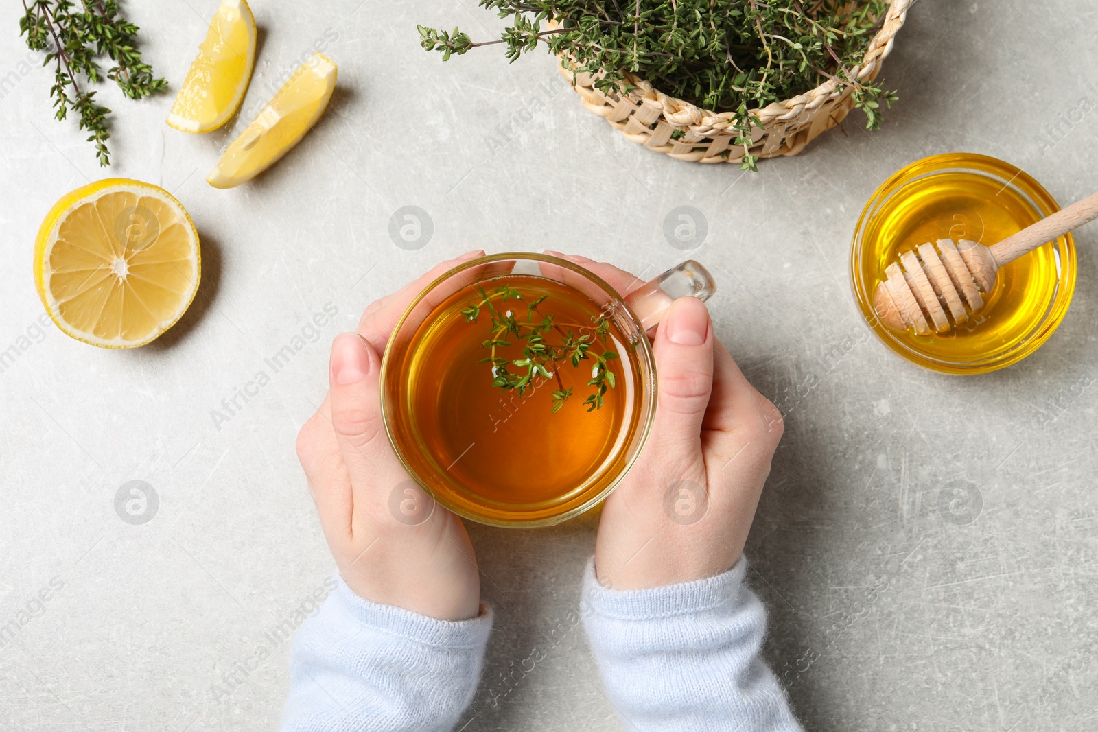 Photo of Woman holding cup of tasty herbal tea with thyme at light grey table, top view