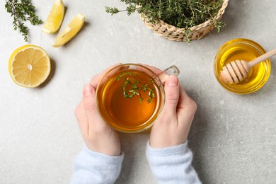 Photo of Woman holding cup of tasty herbal tea with thyme at light grey table, top view