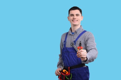 Photo of Young man holding pliers on light blue background, space for text