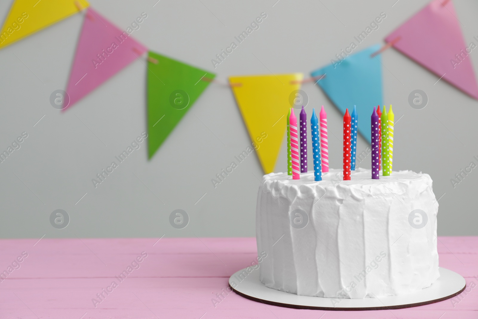 Photo of Delicious cake with cream and candles on pink wooden table. Space for text