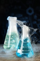 Laboratory glassware with colorful liquids and steam on wooden table against black background, space for text. Chemical reaction