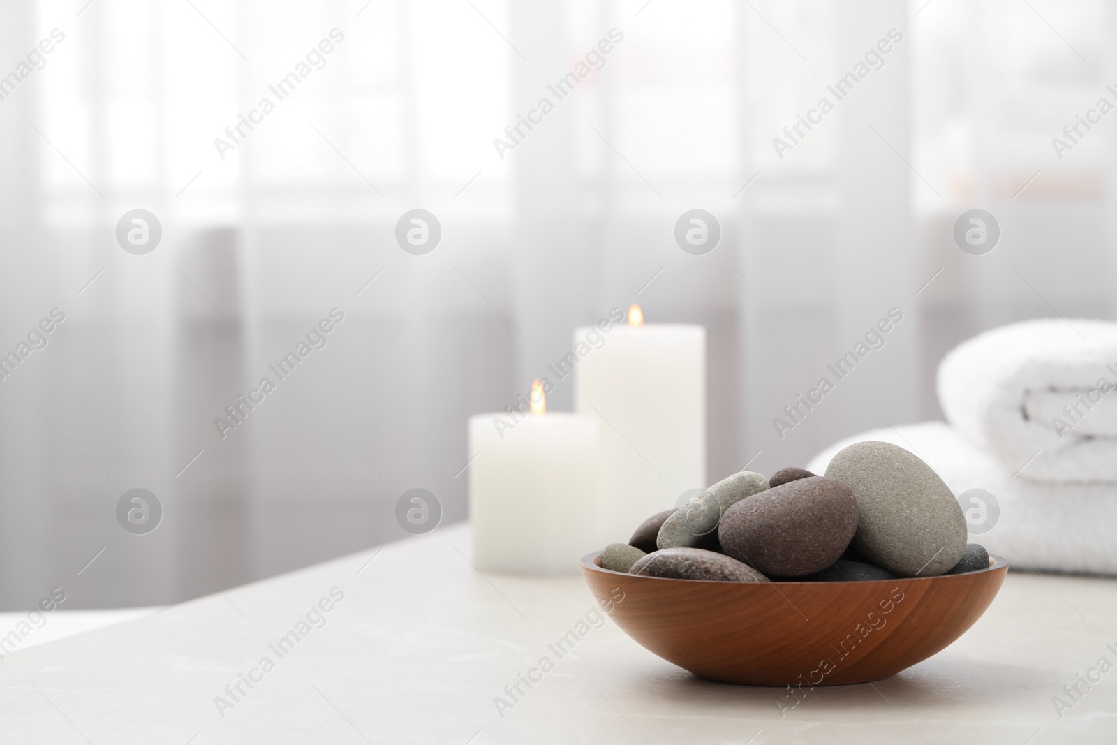 Photo of Spa stones in wooden bowl on white table indoors. Space for text