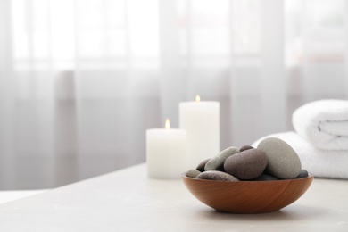 Spa stones in wooden bowl on white table indoors. Space for text