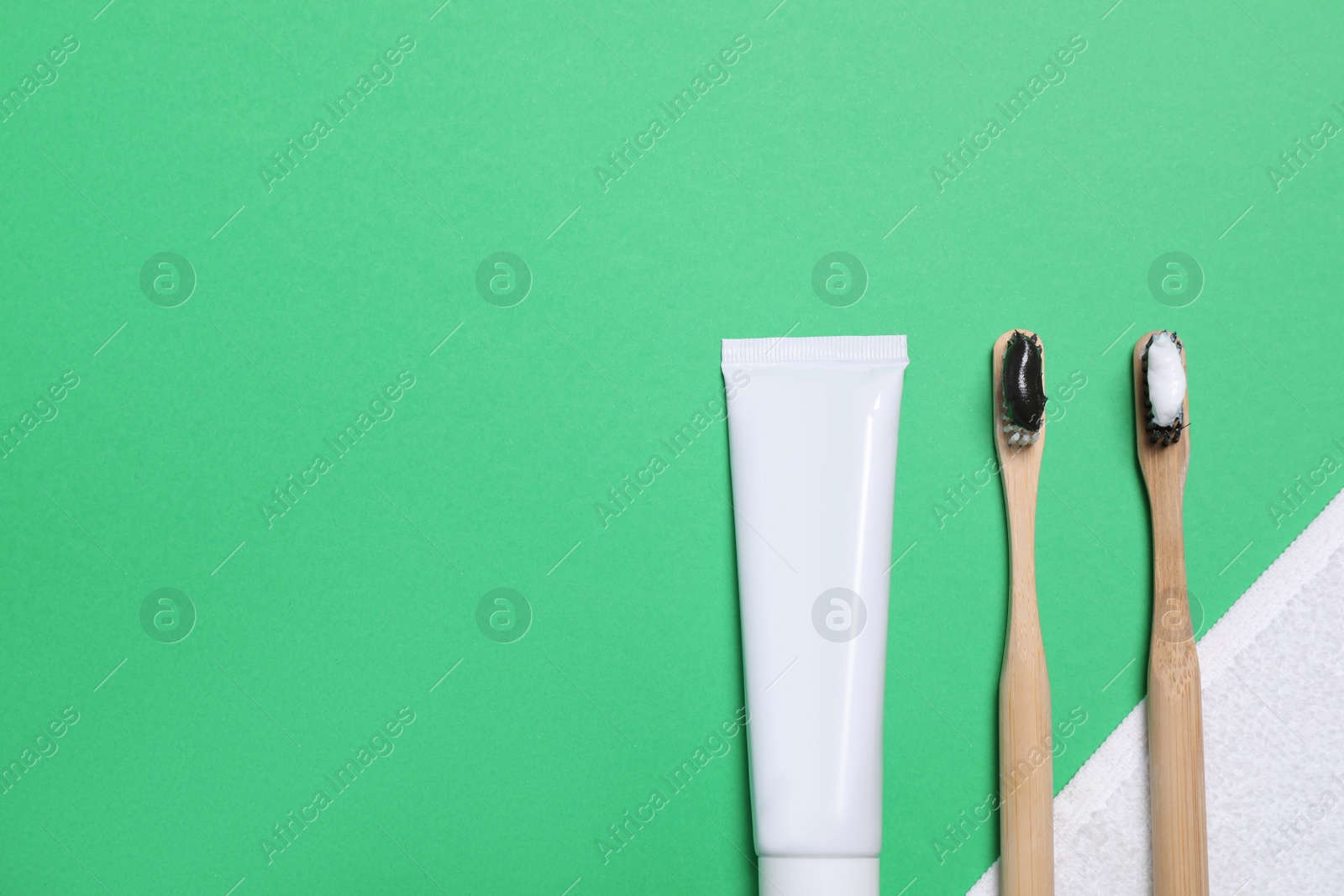 Photo of Toothpaste, brushes and towel on green background, flat lay. Space for text