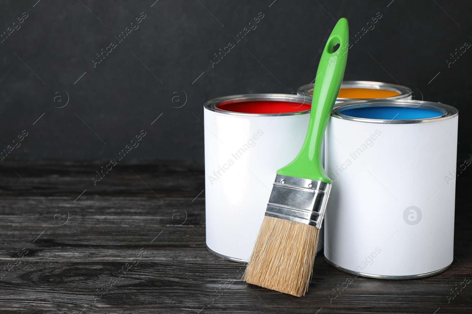 Photo of Cans of paint and brush on black wooden table. Space for text