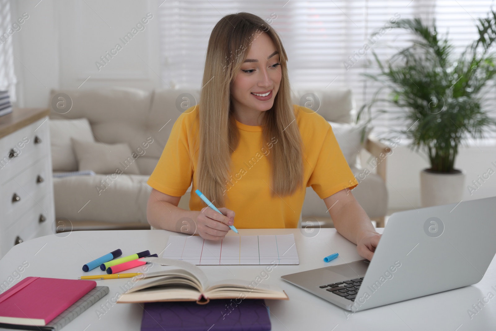 Photo of Young woman watching webinar at table in room