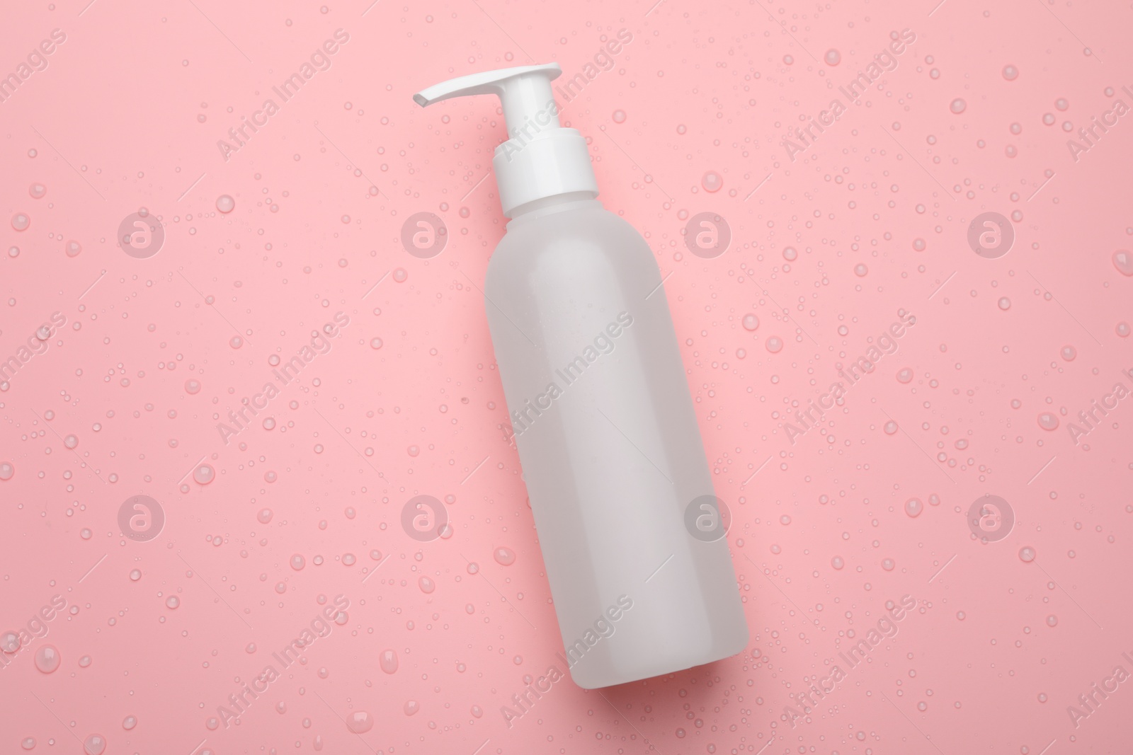 Photo of Wet bottle of face cleansing product on pink background, top view