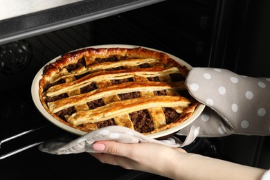 Photo of Woman taking delicious freshly baked meat pie from oven, closeup