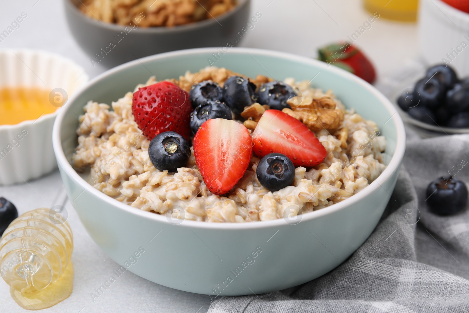 Photo of Tasty oatmeal with strawberries, blueberries and walnuts in bowl on grey table, closeup