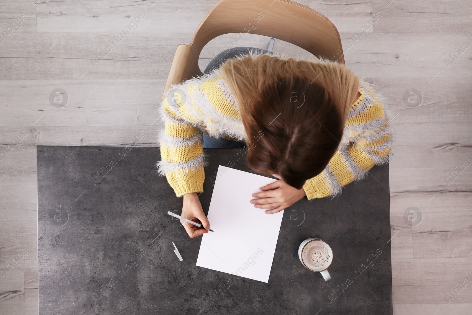 Photo of Woman writing on sheet of paper at table indoors, top view