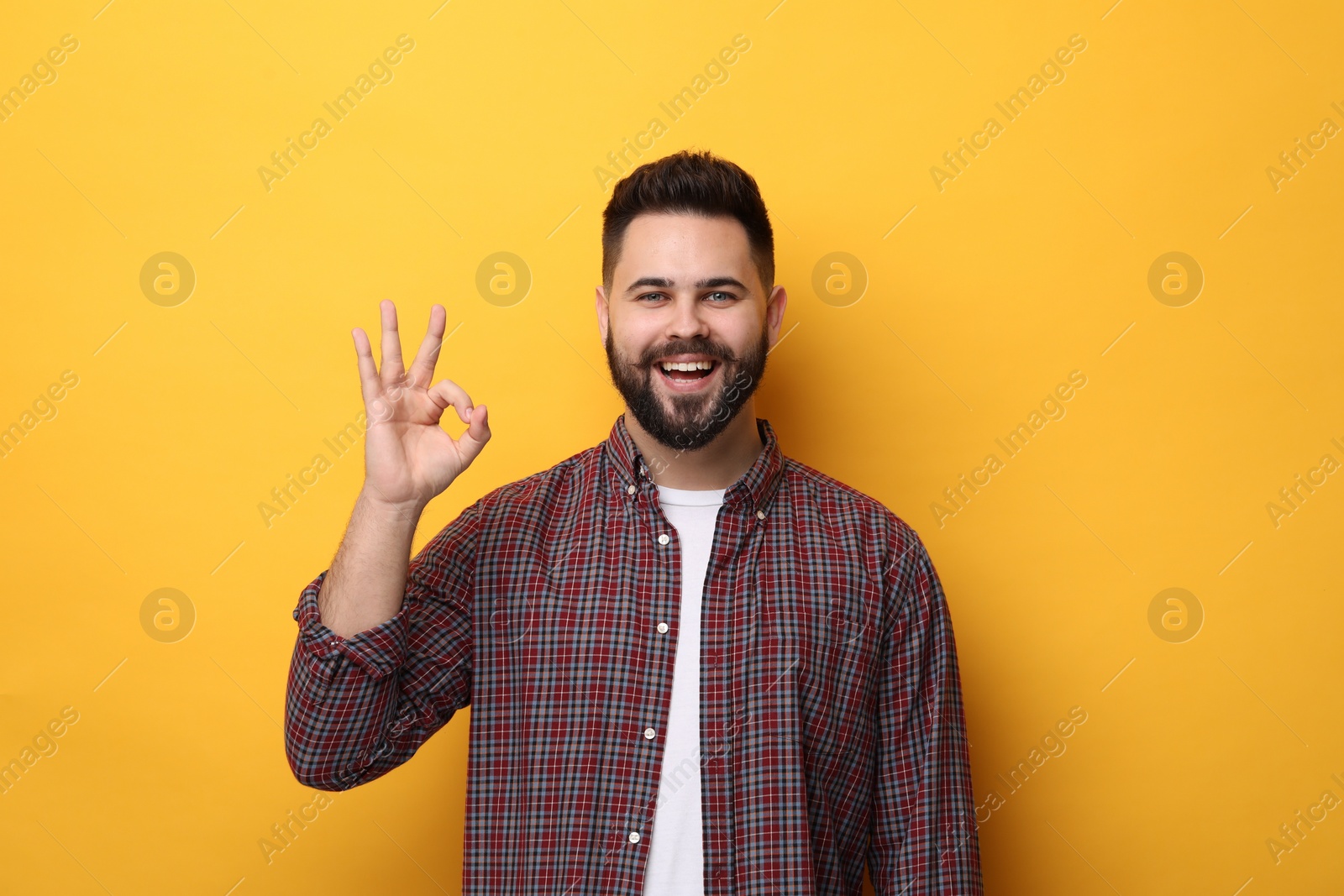Photo of Happy young man with mustache showing OK gesture on yellow background
