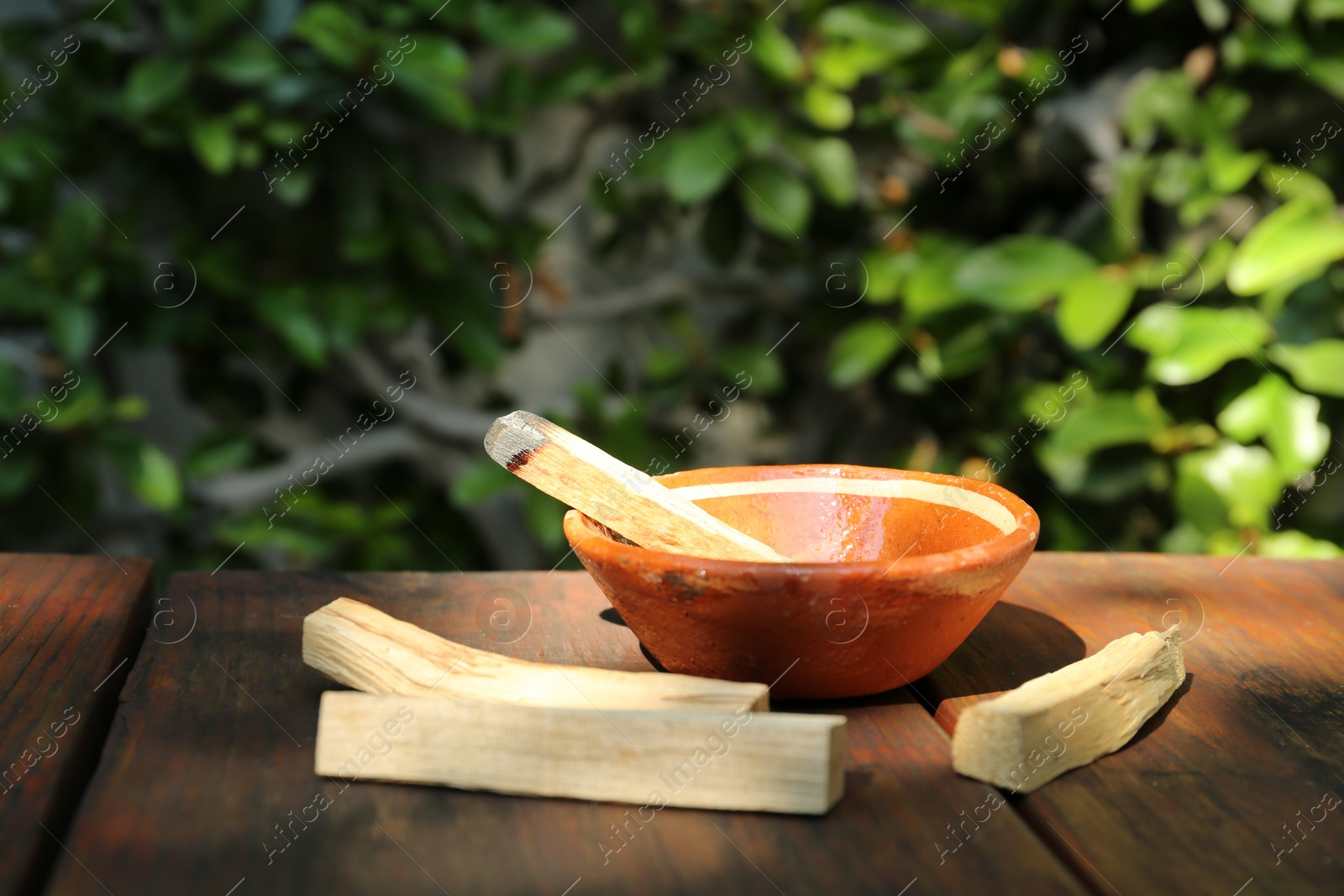Photo of Palo santo sticks and bowl on wooden table outdoors, space for text