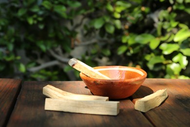 Photo of Palo santo sticks and bowl on wooden table outdoors, space for text