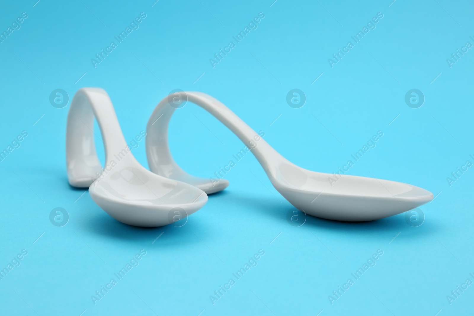 Photo of Clean empty ceramic appetizer spoons on blue background