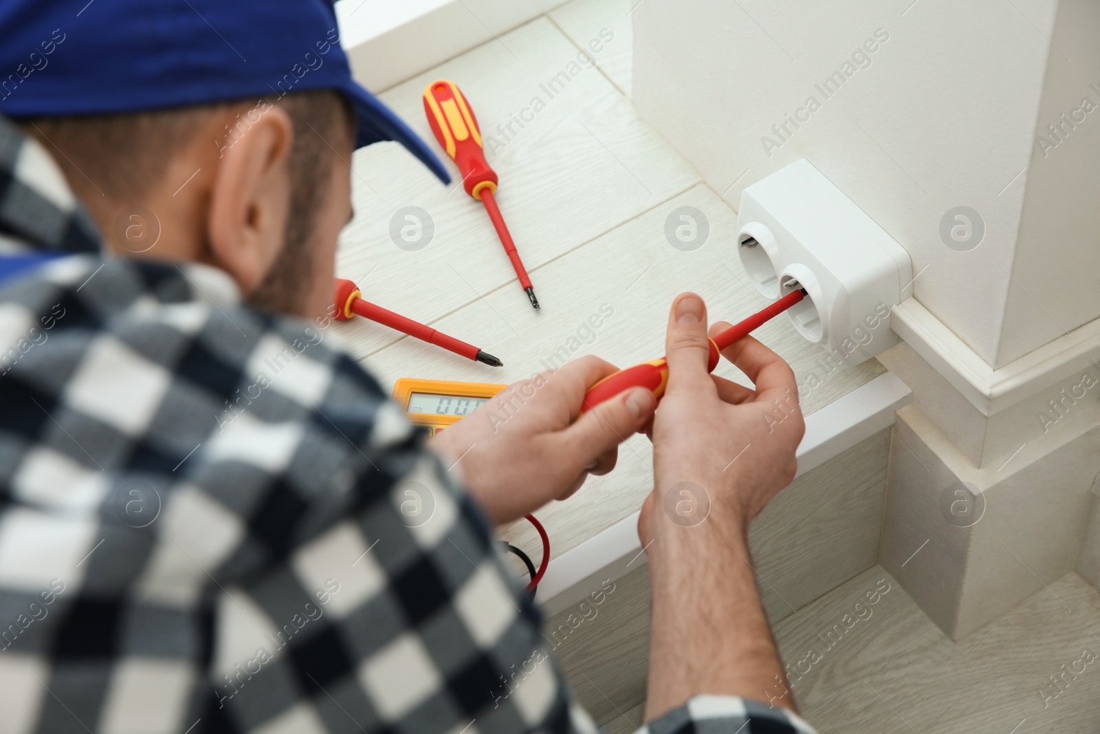 Photo of Electrician with screwdriver repairing power socket indoors, closeup