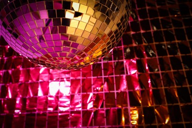 Photo of Shiny disco ball against foil party curtain under pink light. Space for text