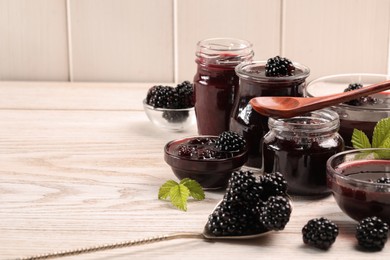 Photo of Tasty blackberry jam and fresh berries on white wooden table. Space for text