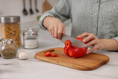 Cooking process. Woman cutting bell pepper at white countertop in kitchen, closeup