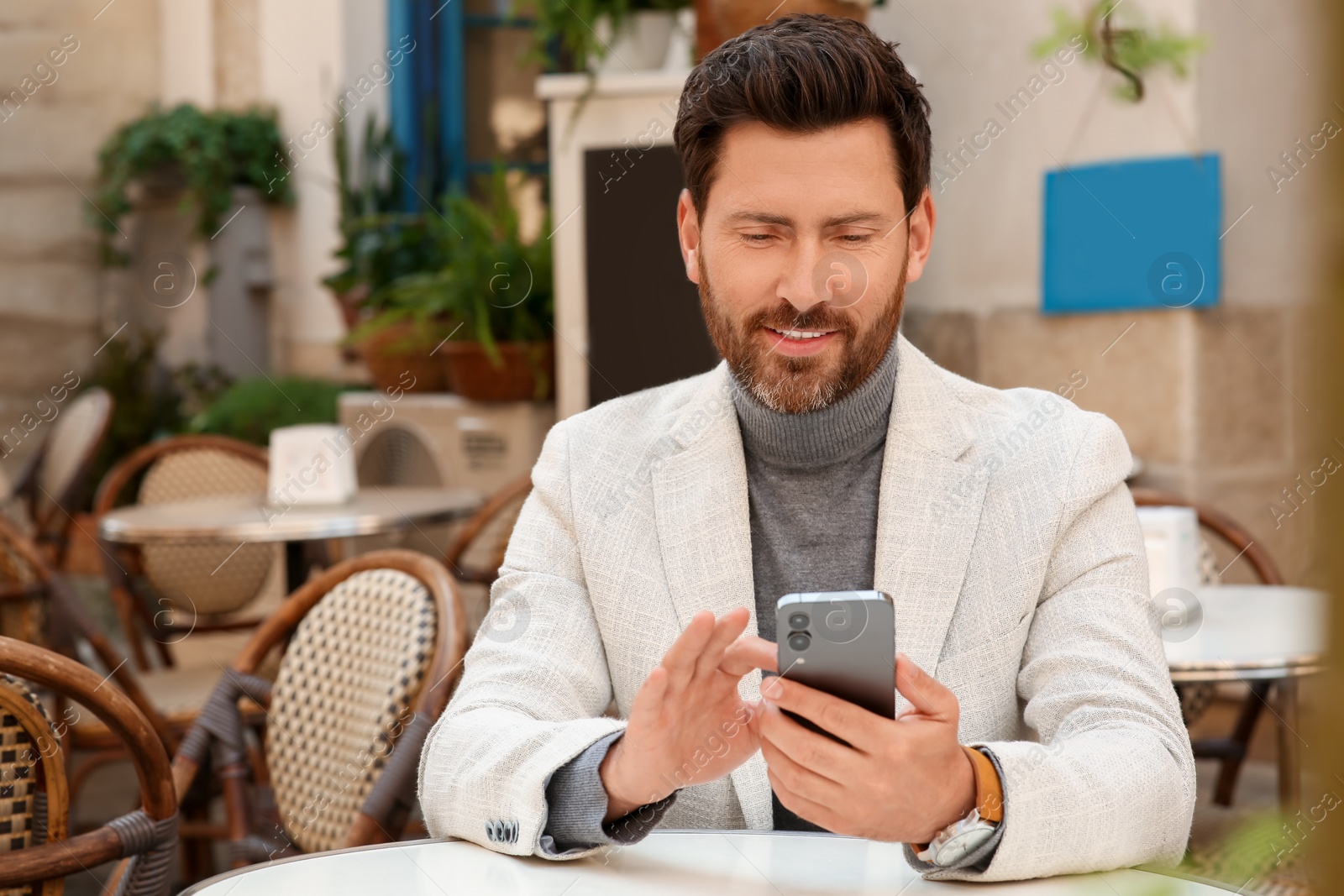 Photo of Handsome man sending message via smartphone at table outdoors